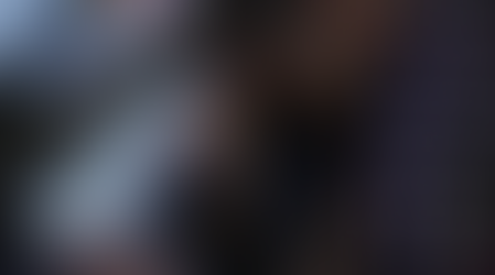 Man in plaid shirt asleep on desk, holding coffee cup. Computer keyboard and screen visible. Mood suggests fatigue or burnout