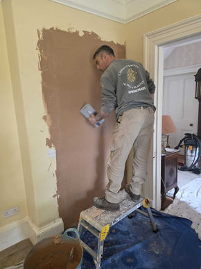 Worker using plastering tools and protective sheets to refine wall surfaces during home renovation project.