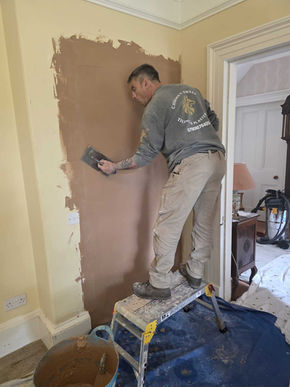Fresh plaster being applied to wall with bucket and tools nearby, highlighting construction and repair work.
