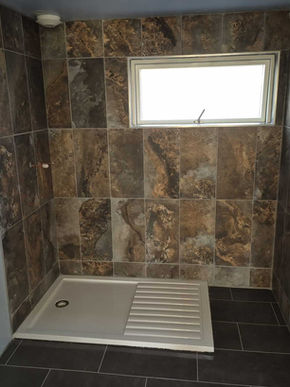 Newly tiled shower area featuring a clean white shower tray, highlighting bathroom renovation and modern installation progress.