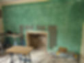 Exposed stone fireplace in a room being renovated with fresh green plaster walls