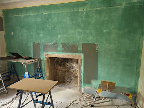 Exposed stone fireplace in a room being renovated with fresh green plaster walls