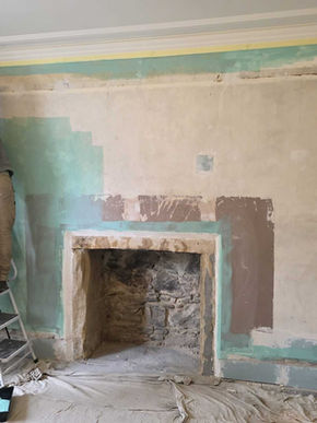 Partially restored fireplace with exposed stone and plaster, showing craftsmanship and ongoing structural restoration efforts.
