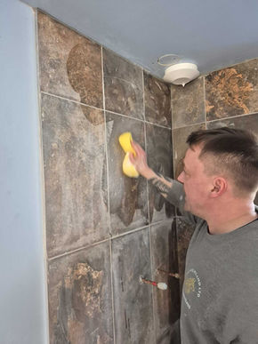 Person cleaning and polishing newly installed shower tiles, ensuring smooth finish and professional quality in bathroom renovation.