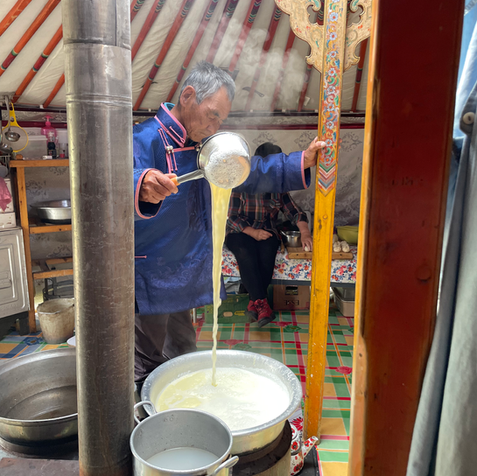 Man in traditional Mongolian robe pouring milk tea in a ger in Mongolia