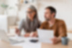 Couple sitting together at computer with paperwork.