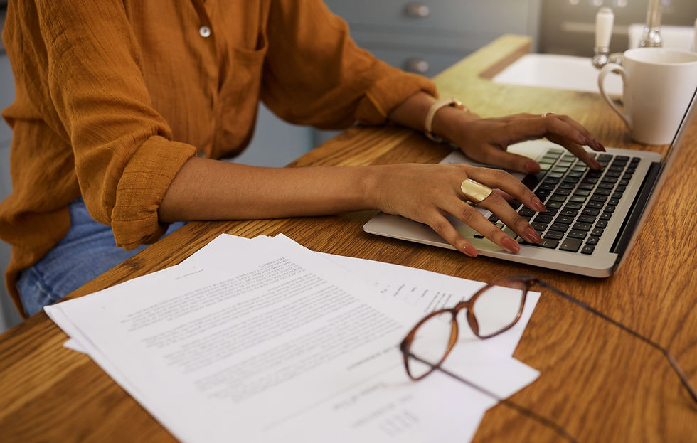 Professional woman typing on her computer next to a pile of documents.