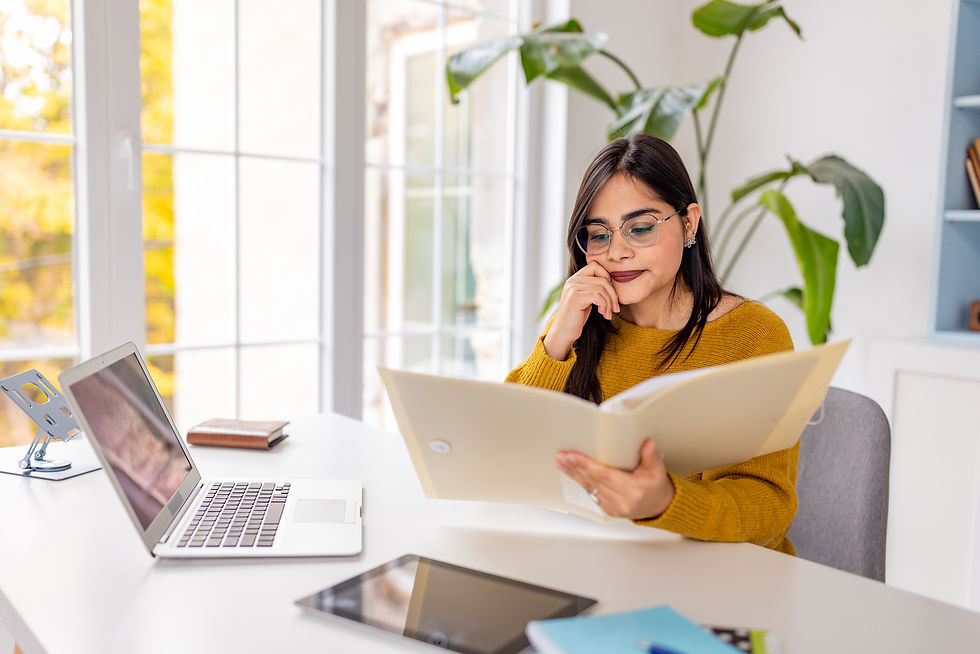 Woman at her computer looking at a file she is holding in her hands.