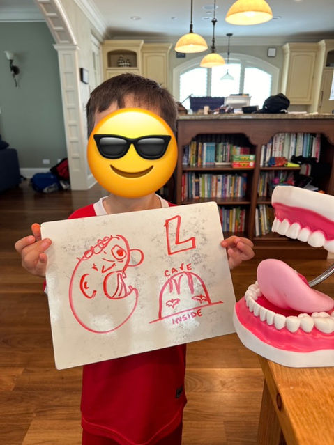 A speech therapy client who is proud of his work is holding a whiteboard with articulation reminders during therapy.