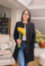 A woman wearing a navy blue handmade coat carrying a bunch of daffodils