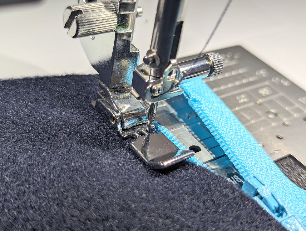 A zip foot on a sewing machine sewing a turquoise zip into a navy blue fabric