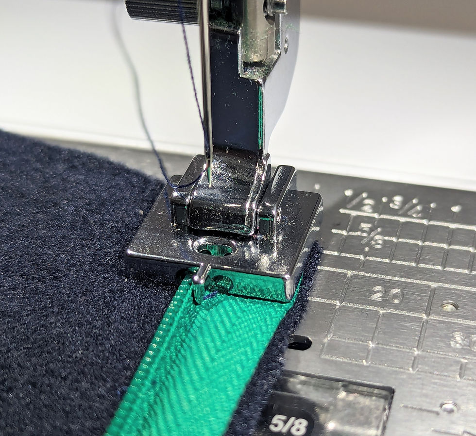 A concealed zip foot on a sewing machine sewing a green zip into a navy blue fabric