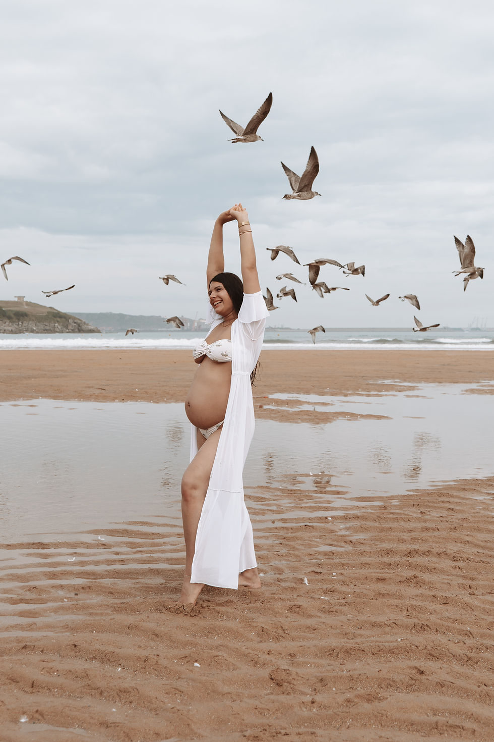 una mujer embarazada en una playa con gaviotas volando de fondo
