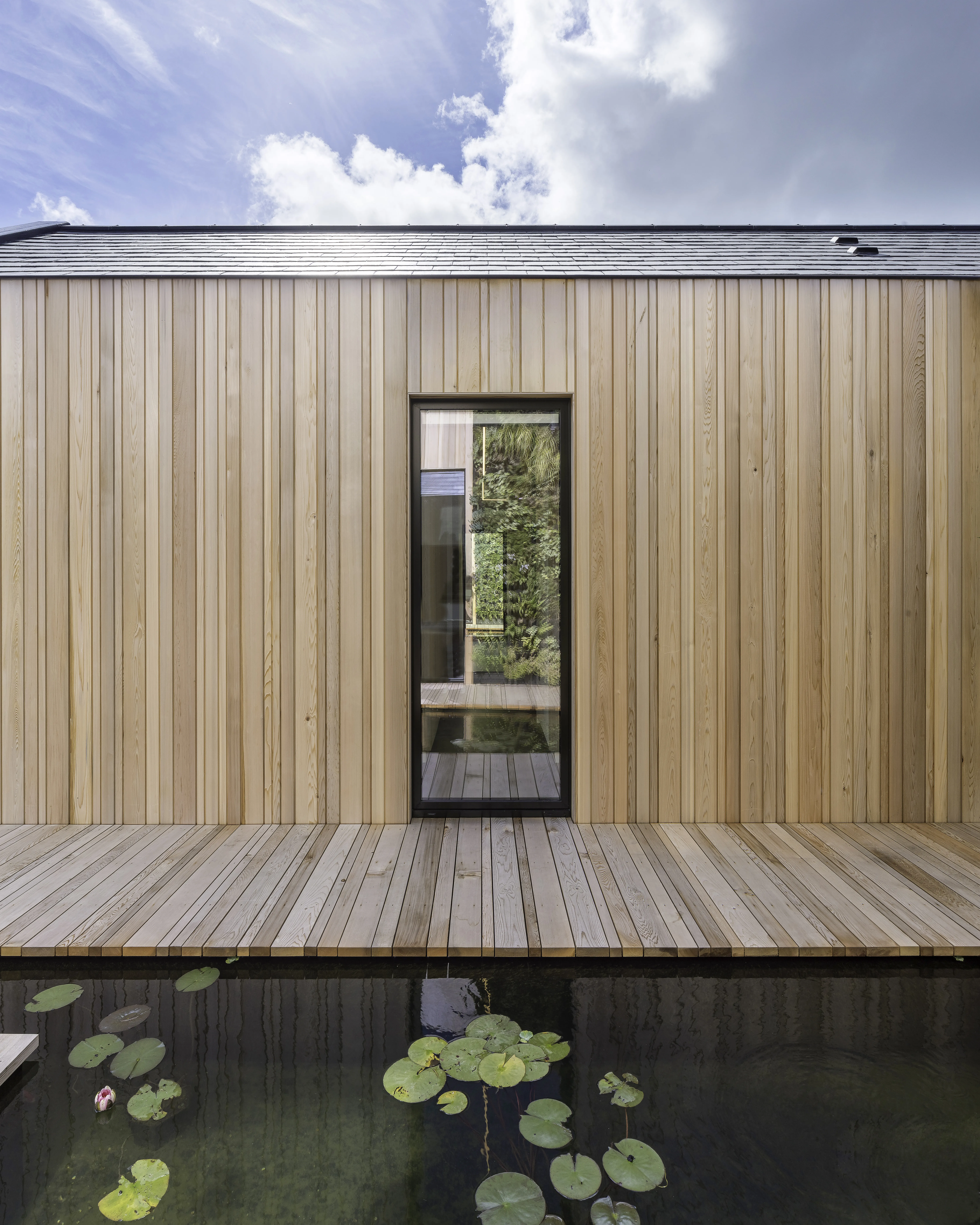 Exterior view of completed residential project with wooden wall and pond in the decking, showcasing DLM Architects' water conservation practices in the design and development process.
