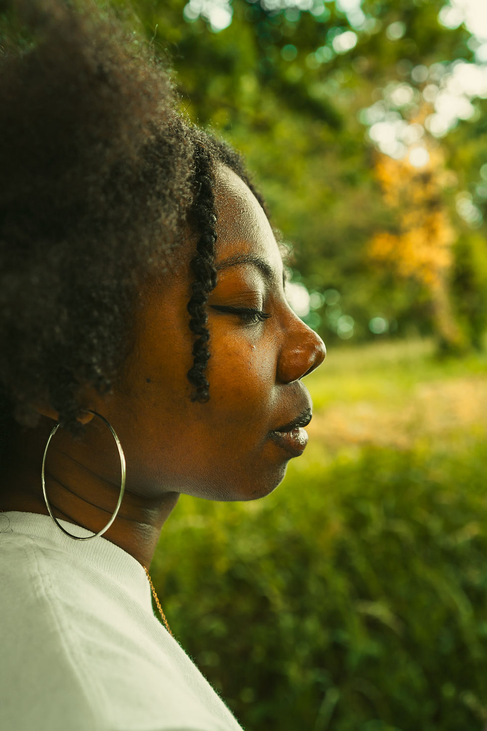 Une femme noire de profil tournée vers la droite, les yeux fermés dans la nature.