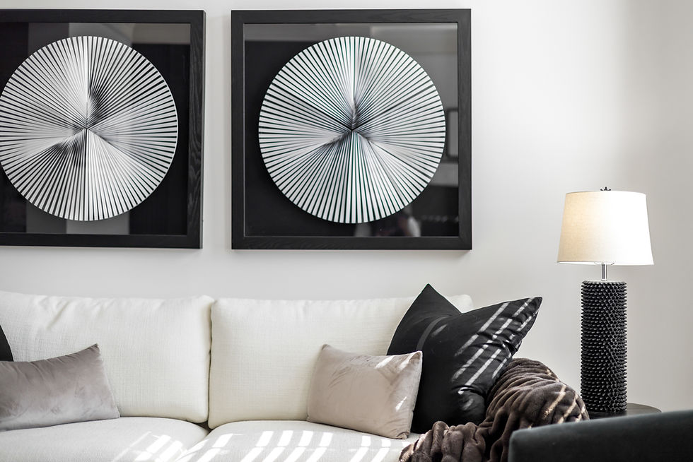 Modern living room with white sofa, black and taupe pillows, textured lamp, and geometric wall art. Cozy atmosphere with soft lighting.