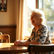 A woman in her 70s sitting at a sunlit table, laughing — warm, natural light, relaxed posture.