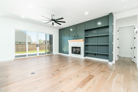 Living room with hardwood floors, sliding glass doors, and green built-in wall with fireplace and open shelving.