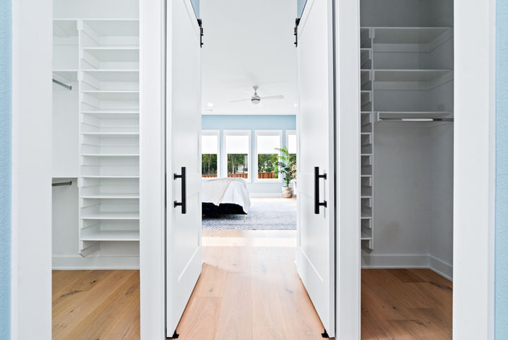 Walk-in closet with custom shelving leading into primary bedroom in Northwest Arkansas home.