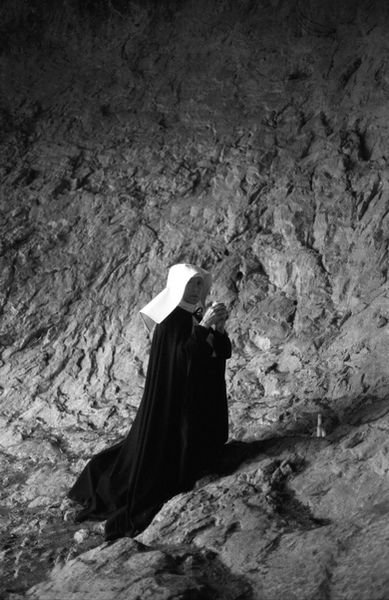 Elderly nun praying inside a stone cave.