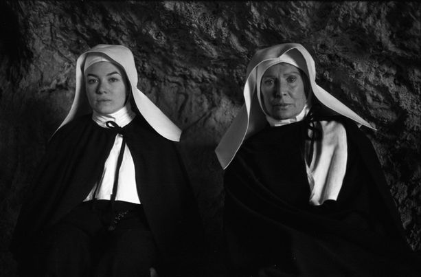 Front portrait of two nuns seated in low light.