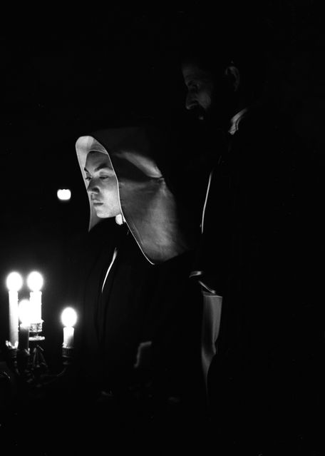 Nun and priest beside a lit candelabrum.