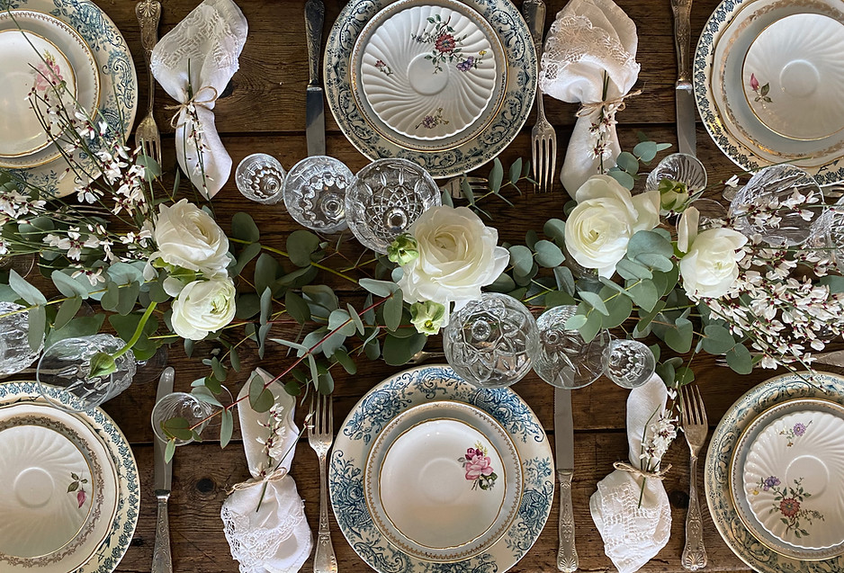 Table dressée, chaque couvert dispose de 3 assiettes, un modèle terre de fer en assiette plate, un modèle doré en assiette à entremet, un modèle bucolique en assiette à pain. De chaque côté on dispose les couverts en argent. Il y a trois verres ciselés par convive. Une composition florale orne le centre de la magnifique table en bois. La composition est faite de branches fraîche d’eucalyptus, de renoncules blanches. Estuaire, Saint Emilion, Bassin d’Arcachon, verre en cristal, dresser la table, convive, repas, gastronomie, cuisine, amour, passion.