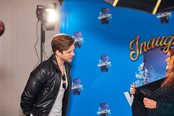 Male actor greeting female fan for professional photo in front of event backdrop.