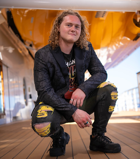 Man with long curly hair crouching on a ship deck, smiling