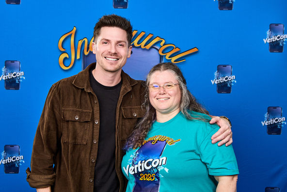 An male actor and female posing for professional photo in front of a blue even backdrop.