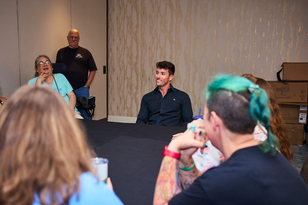 Male actor at a table, surrounded by fans, during a meet and greet meeting. 