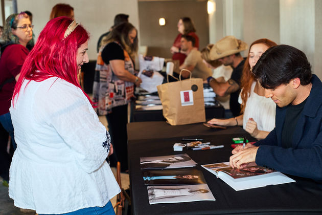 Female fan smiling down at seated male actor as he signs autograph.