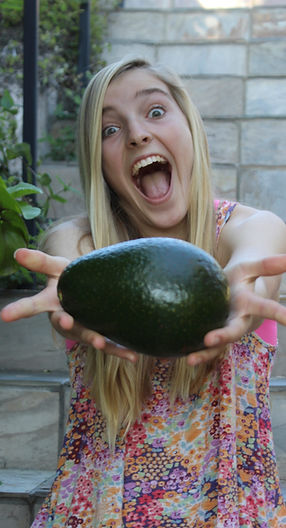 a blond teenager holding a large green avocado
