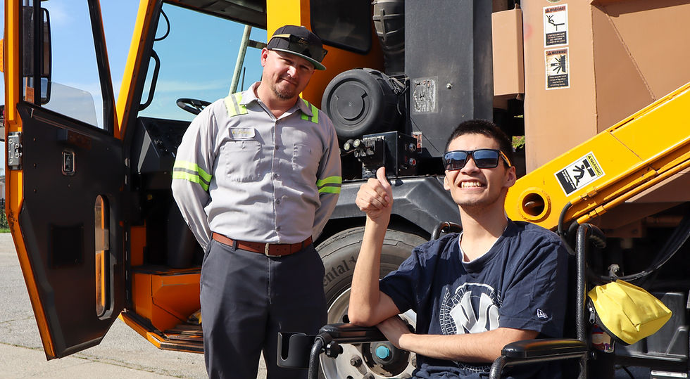 A worker and a smiling man in a wheelchair by a crane.