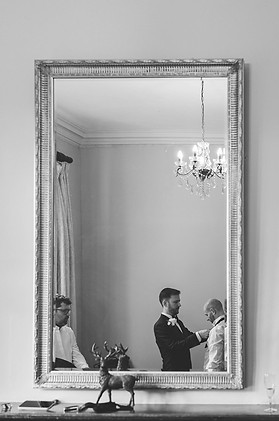 Reflection in mirror of groom helping best man with tie at Highley Manor