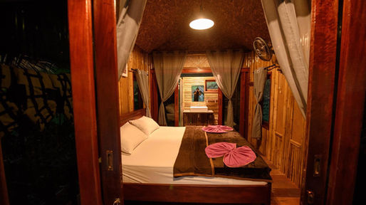 Deluxe bamboo floating room at Praiwan Raft House on Cheow Lan Lake, featuring natural wooden interiors, private bathroom, and tranquil rainforest surroundings in Khao Sok National Park.