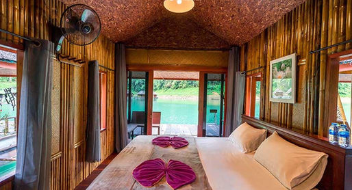 Deluxe bamboo floating room at Praiwan Raft House on Cheow Lan Lake, featuring natural wooden interiors, private bathroom, and tranquil rainforest surroundings in Khao Sok National Park.