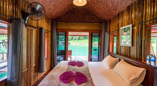 Deluxe bamboo floating room at Praiwan Raft House on Cheow Lan Lake, featuring natural wooden interiors, private bathroom, and tranquil rainforest surroundings in Khao Sok National Park.