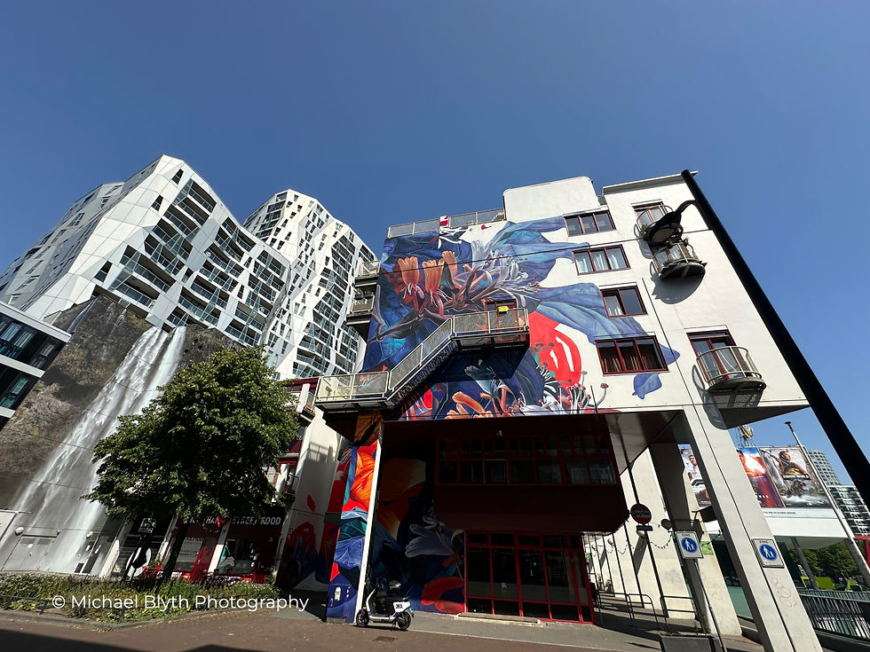 Colorful street mural on a building with modern high-rises in the background, set against a clear blue sky. Bright and vibrant urban scene. Rotterdam