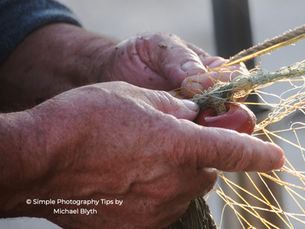 Close-up of weathered hands carefully untangling a fishing net in warm evening light.