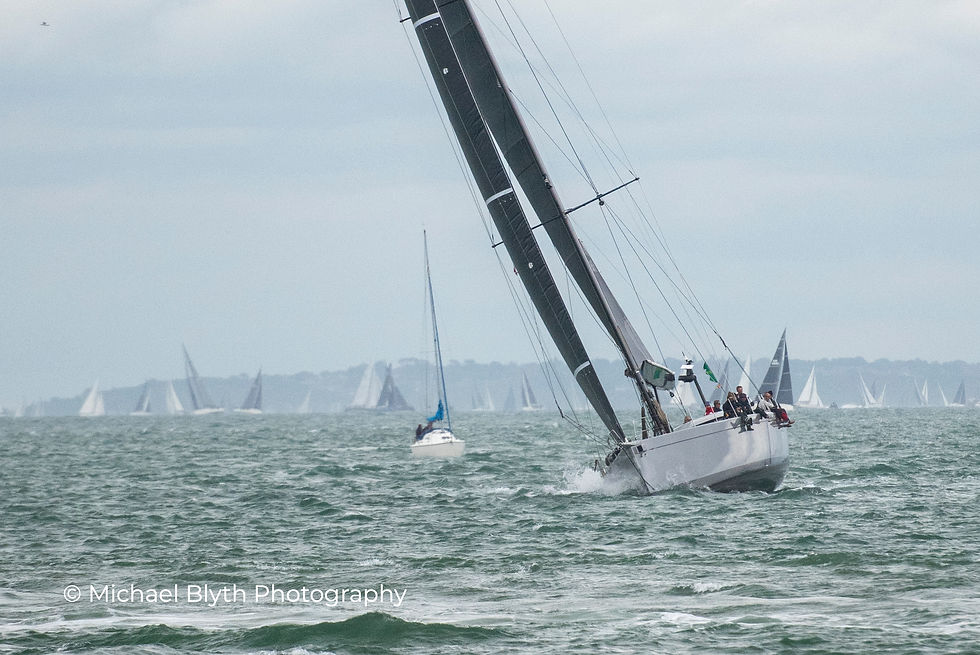 Fastnet race 2025, yacht La Loévie, choppy sea under cloudy skies. Main boat tilts dramatically with crew onboard. Distant sails fill the horizon.