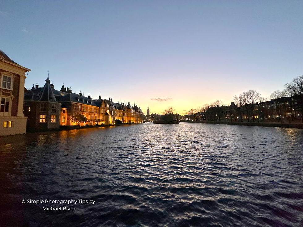 Binnenhof parliament buildings in The Hague reflected in the Hofvijver lake at dusk with warm architectural lighting contrasting against the fading evening sky.