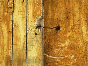 Weathered yellow wooden door with peeling paint and an old metal latch, photographed in soft natural light