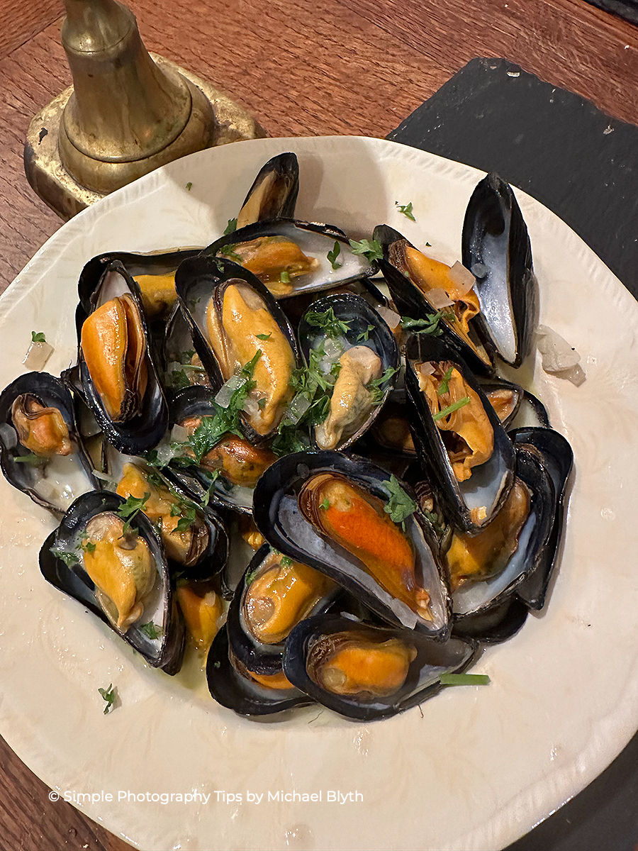 Steamed mussels served on a white plate photographed with a wide field of view to show the full dish and table setting.