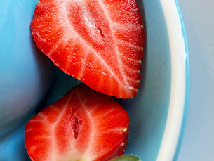 A strawberry cut in half and placed in a blue bowl, suggesting the simple act of sharing.
