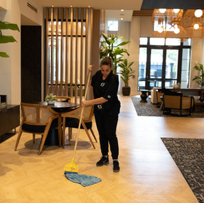 Woman wearing a black cleaning uniform mopping the floor of a lobby.