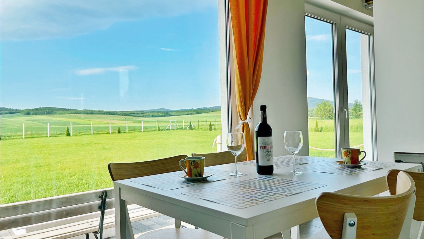 Widok z kuchennego stołu w Nuka House na zielone pola, wzgórza i Biskupią Kopę przez panoramiczne okna.
