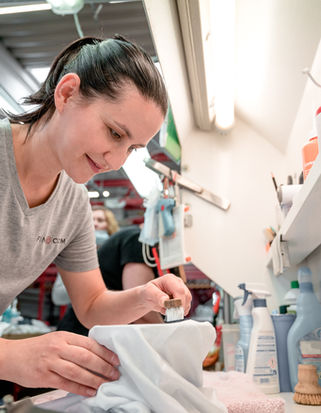 Auf dem Bild sieht man eine Mitarbeiterin, die mithilfe einer Bürste Flecken von einem Kleidungsstück entfernt