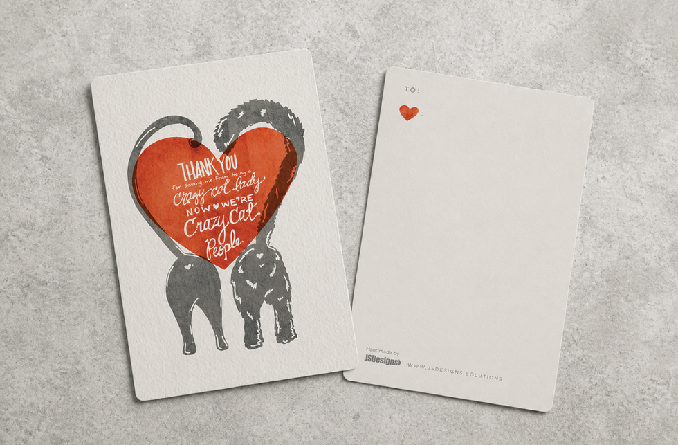 Valentine card with two cats forming a heart and humorous message about being crazy cat people, shown with back side on textured gray surface