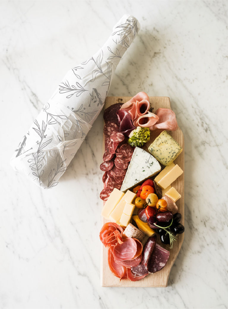 Custom wine bottle wrapped in branded botanical paper next to a charcuterie board on marble surface